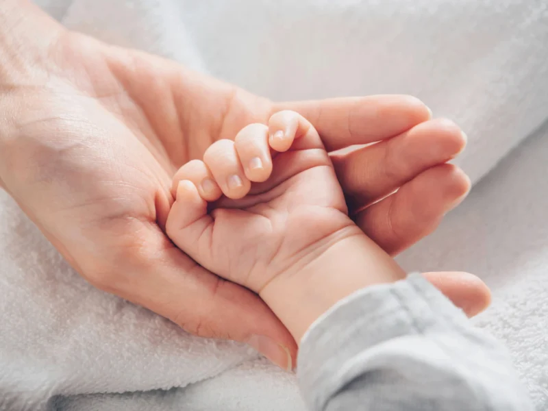 A woman holding a small baby's hand.