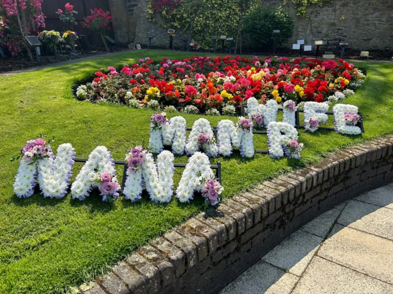 Three rows of funeral flowers reading Nana, Mam & Wife.