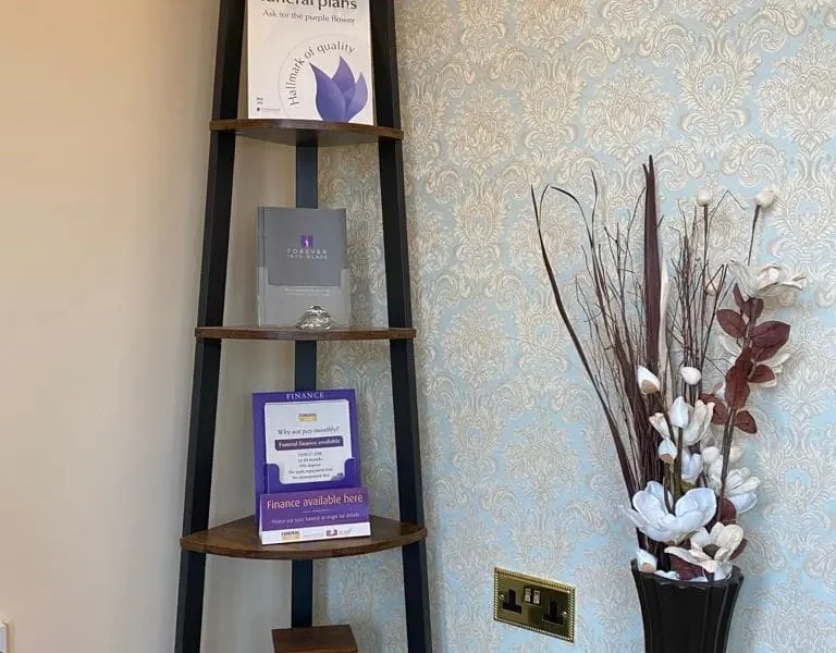 A triangular shelving unit next to some flowers.