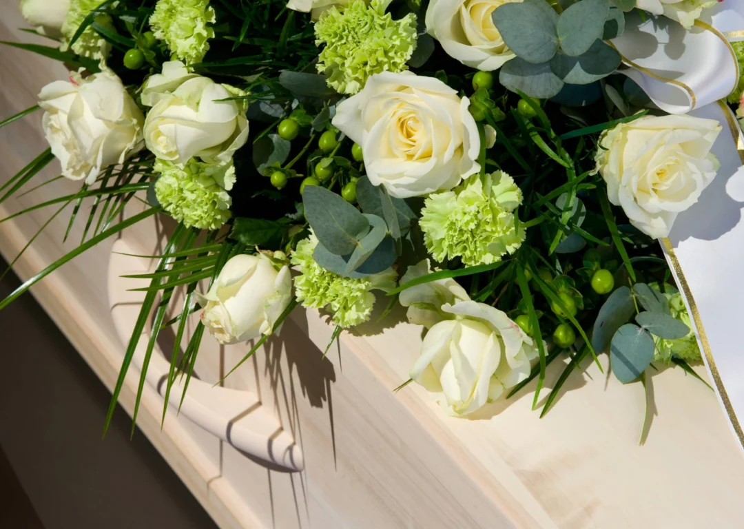 A white coffin with green and white flowers on top.