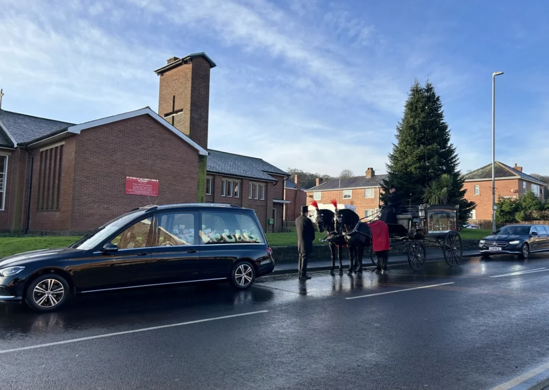 A hearse, limo and carriage outside a crematorium.