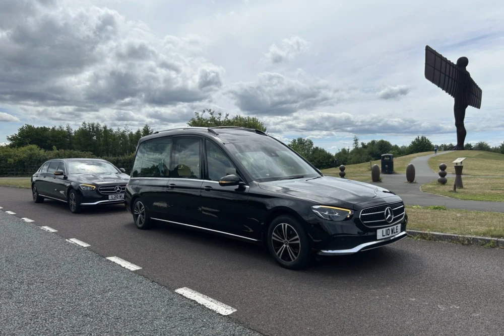 A black Mercedes hearse and limo driving past the Angel of the North.