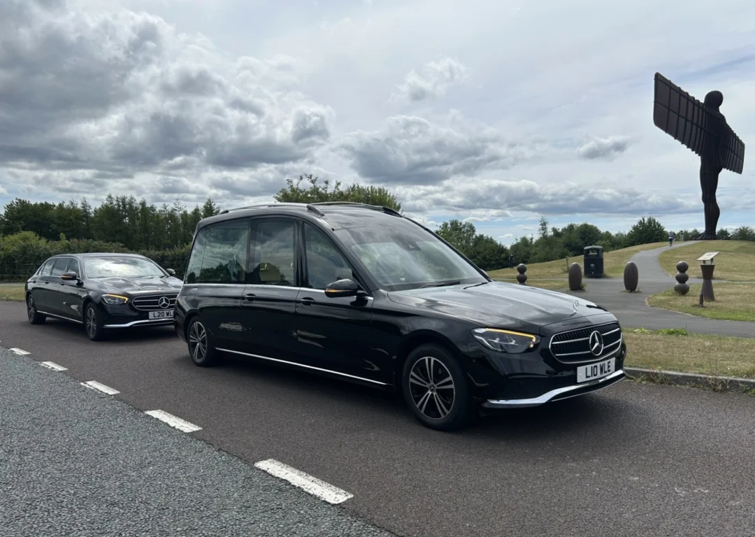 A black Mercedes hearse and limo driving past the Angel of the North.