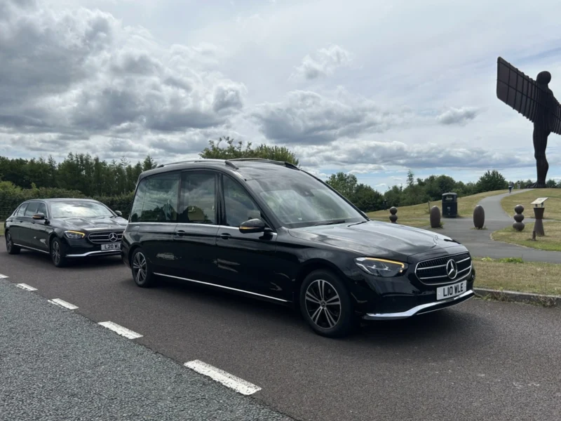 A black Mercedes hearse and limo driving past the Angel of the North.