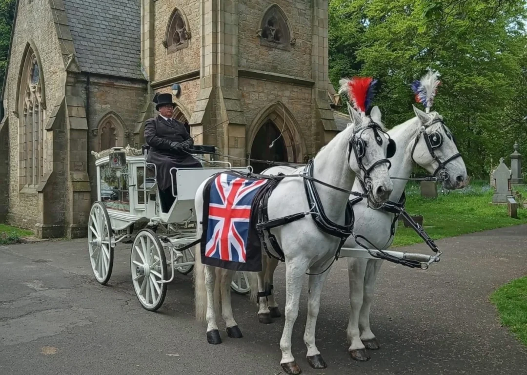 A white horse-drawn carriage with a Union flag draped over the horses.