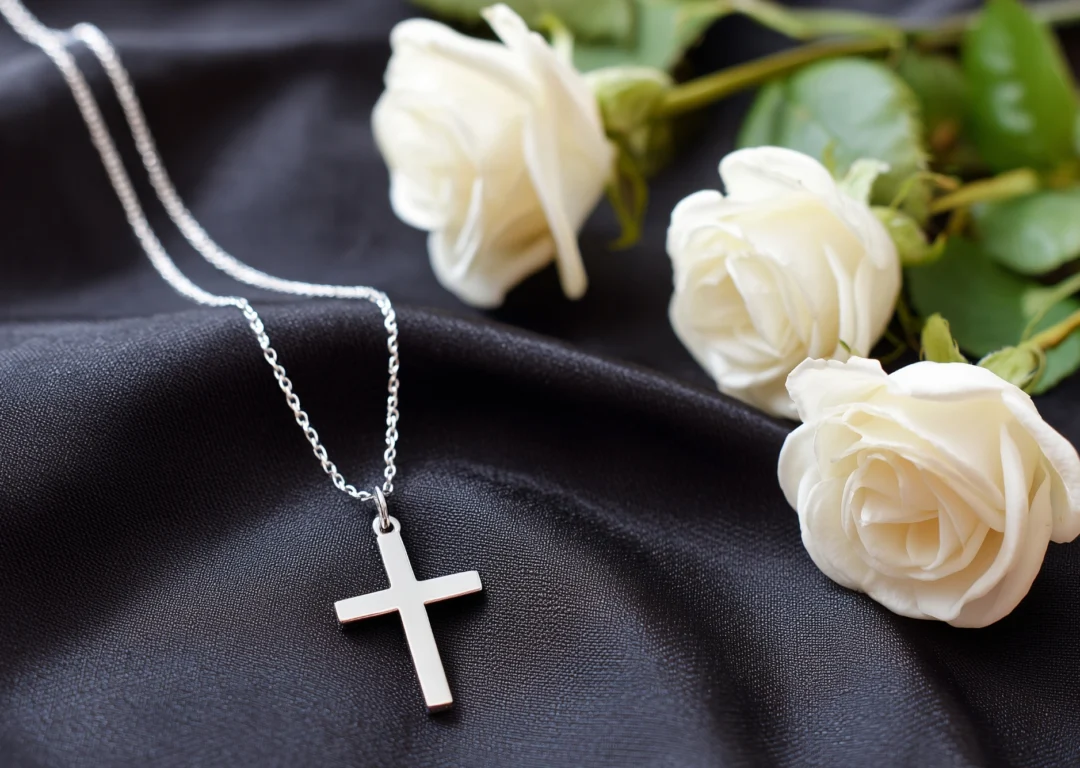 A silver cross necklace lying next to white roses.