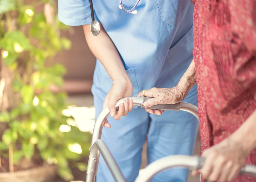 A nurse helping a care home resident with her zimmerframe.