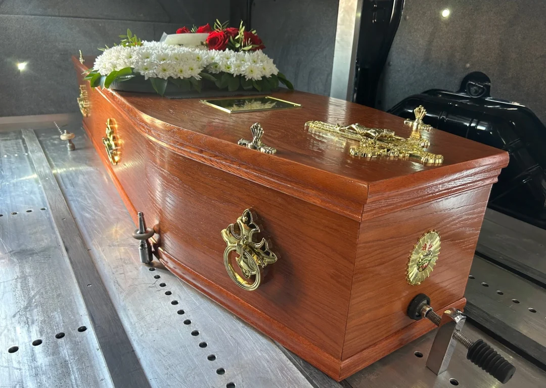 A wooden coffin adorned with flowers in the back of a vehicle.
