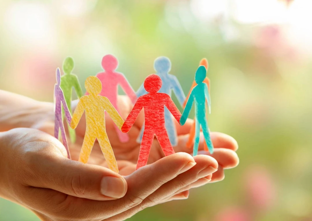 A pair of hands holding paper cut-outs of little people.